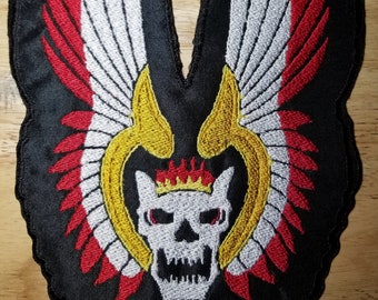 May include: Black embroidered patch with a white skull wearing a gold crown with flames. The skull is surrounded by red and white wings.