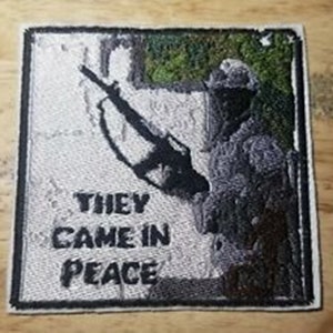 May include: A black and white embroidered patch with a soldier holding a rifle. The text "They came in peace" is embroidered on the patch.