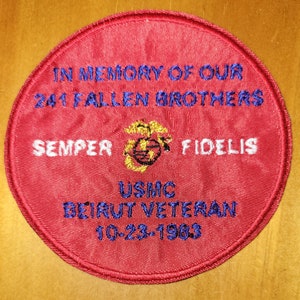 May include: A red circular patch with white and blue embroidered text. The text reads "In Memory of Our 241 Fallen Brothers Semper Fidelis USMC Beirut Veteran 10-23-1983". A gold embroidered emblem of the Marine Corps globe and anchor is centered above the text.