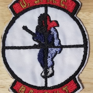 May include: A white embroidered patch with a red and black border. The patch features a black silhouette of a soldier holding a rifle, with a red target in the background. The text "U.S.M.C." is embroidered in gold on a red banner at the top of the patch, and the text "BEIRUT" is embroidered in gold on a red banner at the bottom of the patch.
