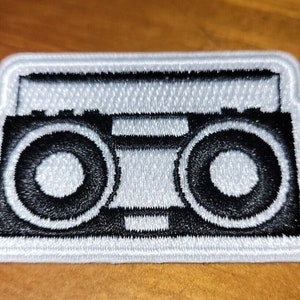 May include: A white embroidered patch of a black and white boombox.