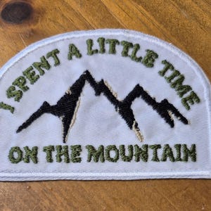 Peut inclure: Patch brodé blanc avec du texte vert qui dit "J'ai passé un peu de temps sur la montagne". Le patch présente une silhouette de montagne noire.