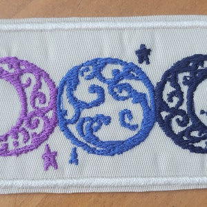 May include: Embroidered patch featuring three crescent moons in purple, blue, and navy blue, each with a star. The moons have intricate designs and are set against a light beige background with a white border.