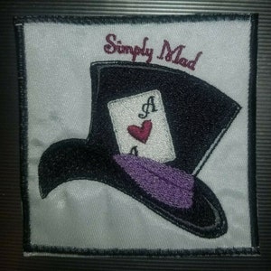May include: Embroidered patch featuring a black top hat with a purple band and an ace of hearts playing card. The text "Simply Mad" is stitched above the hat.