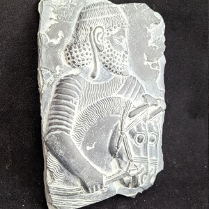 May include: A gray stone relief sculpture of a man on horseback. The man is wearing a helmet and armor, and the horse has a bridle. The sculpture is carved in a detailed style.