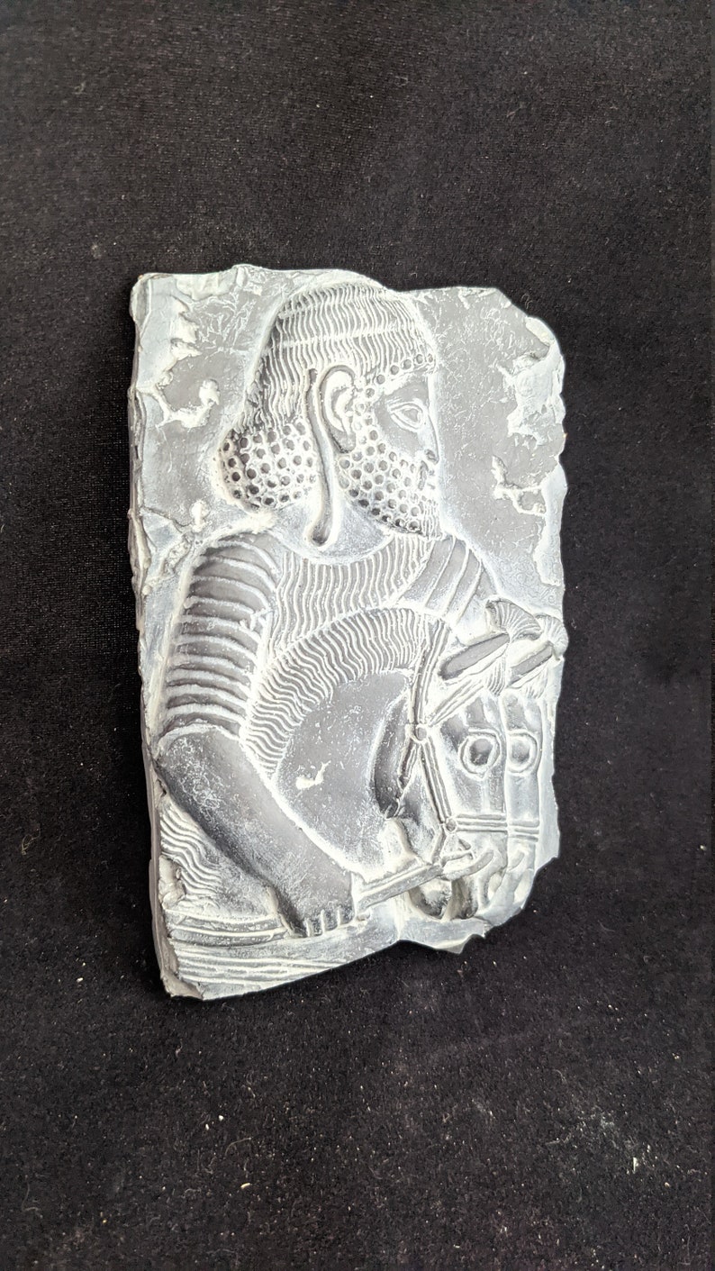 May include: A gray stone relief sculpture of a man on horseback. The man is wearing a helmet and armor, and the horse has a bridle. The sculpture is carved in a detailed style.