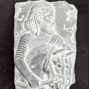 May include: A white plaster relief sculpture of a man on horseback. The man is wearing a helmet and armor, and the horse is wearing a bridle. The sculpture is set against a dark background.