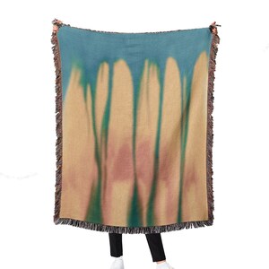 May include: A woven throw blanket with a tie-dye pattern in shades of blue, green, and brown. The blanket has fringe on all sides.