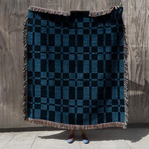 May include: A blue and black woven throw blanket with a checkered pattern and fringe trim.