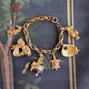 May include: A gold charm bracelet with a variety of sea-themed charms, including a fish, a seahorse, a mermaid, a turtle, and a seashell. The charms are all detailed and have a vintage look.