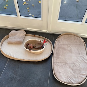 May include: Two oval-shaped pet beds made of natural jute rope with a beige fabric lining. One bed has a small white bowl with a red and green rope toy inside.