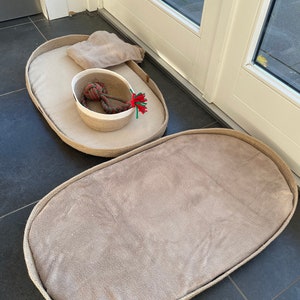 May include: Two oval-shaped pet beds made of woven rope with a beige fabric lining. The smaller bed has a white woven basket with a red and green rope toy inside.
