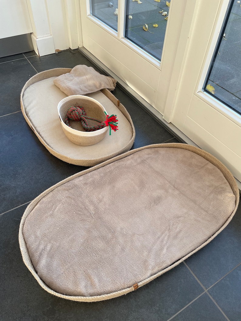 May include: Two oval-shaped pet beds made of woven rope with a beige fabric lining. The smaller bed has a white woven basket with a red and green rope toy inside.