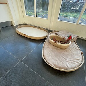 May include: Two oval-shaped pet beds made of natural rope with beige fabric lining. The larger bed has a smaller rope basket inside.