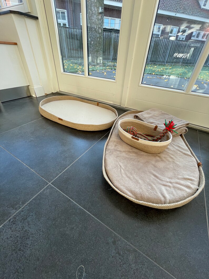 May include: Two oval-shaped pet beds made of natural rope with beige fabric lining. The larger bed has a smaller rope basket inside.