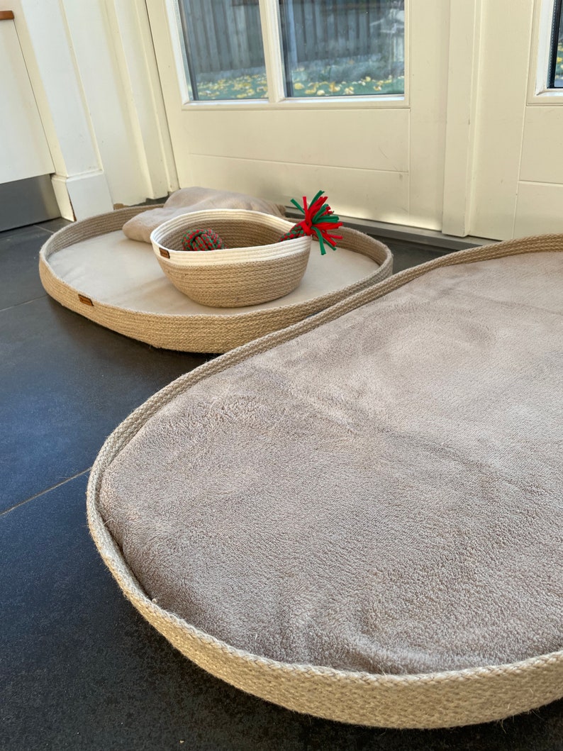 May include: Two oval-shaped pet beds made of natural rope with a soft, beige fabric lining. The smaller bed has a woven rope basket with a white rim inside.