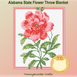 Puede incluir: Un patrón de punto de cruz para una manta de tiro con la flor del estado de Alabama, una camelia rosa con hojas verdes. El patrón está enmarcado con un borde rosa e incluye el texto "TC Counted Cross Stitch Patterns".