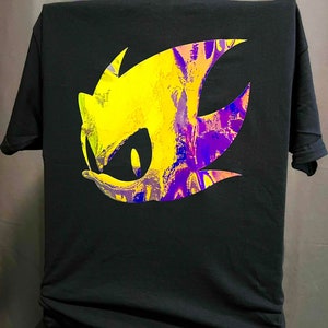 May include: Black t-shirt featuring a vibrant graphic of a character's head with yellow, purple, and blue hues. The design is a stylized illustration of a character's face, with a prominent eye and spiky hair.