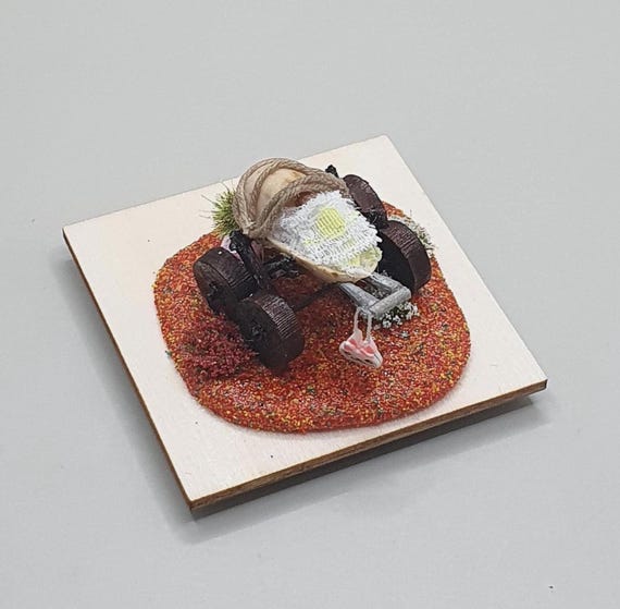 A working doll's pram/stroller built entirely inside a pistachio shell — the kind of micro-diorama that makes people do a double-take and immediately show everyone nearby.