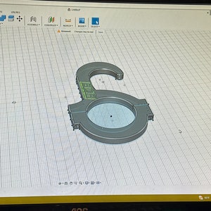 May include: A 3D model of a gray metal hook with a circular opening. The hook is designed for hanging objects. The model is displayed on a computer screen with a grid background.