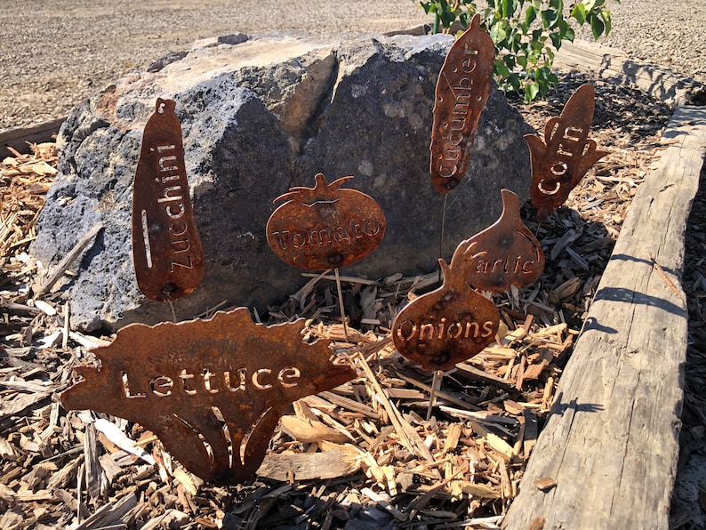 May include: Rustic metal garden markers with the names of vegetables: Zucchini, Tomato, Cucumber, Corn, Garlic, Onions, and Lettuce.