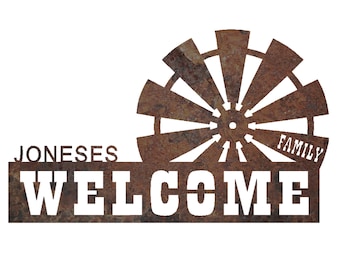 May include: A rustic metal sign with a windmill design and the words "JONESES WELCOME FAMILY" cut out in white. The sign has a weathered, brown finish, suggesting outdoor use.