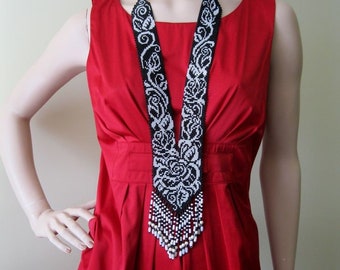 May include: A long black and white beaded necklace with a floral design. The necklace is worn by a mannequin wearing a red dress.