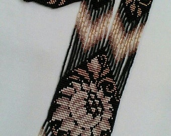 May include: A beaded necklace with a floral design and fringe. The necklace is black with brown and white beads.