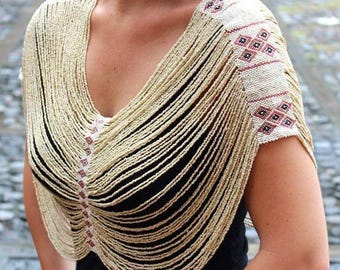 Puede incluir: Un chal blanco de cuentas con un patrón geométrico en rojo y blanco. El chal se lleva sobre una blusa negra.