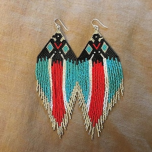 May include: A pair of long, beaded earrings with a geometric pattern in black, white, turquoise, and red. The earrings are made of seed beads and have a fringe-like design.