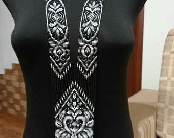 May include: A long black and white beaded necklace with a geometric pattern. The necklace is made of small beads and has a diamond-shaped pendant.