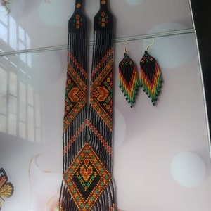May include: A long black beaded necklace with orange, red and green geometric patterns and matching earrings. The necklace has a fringe of beads at the bottom.