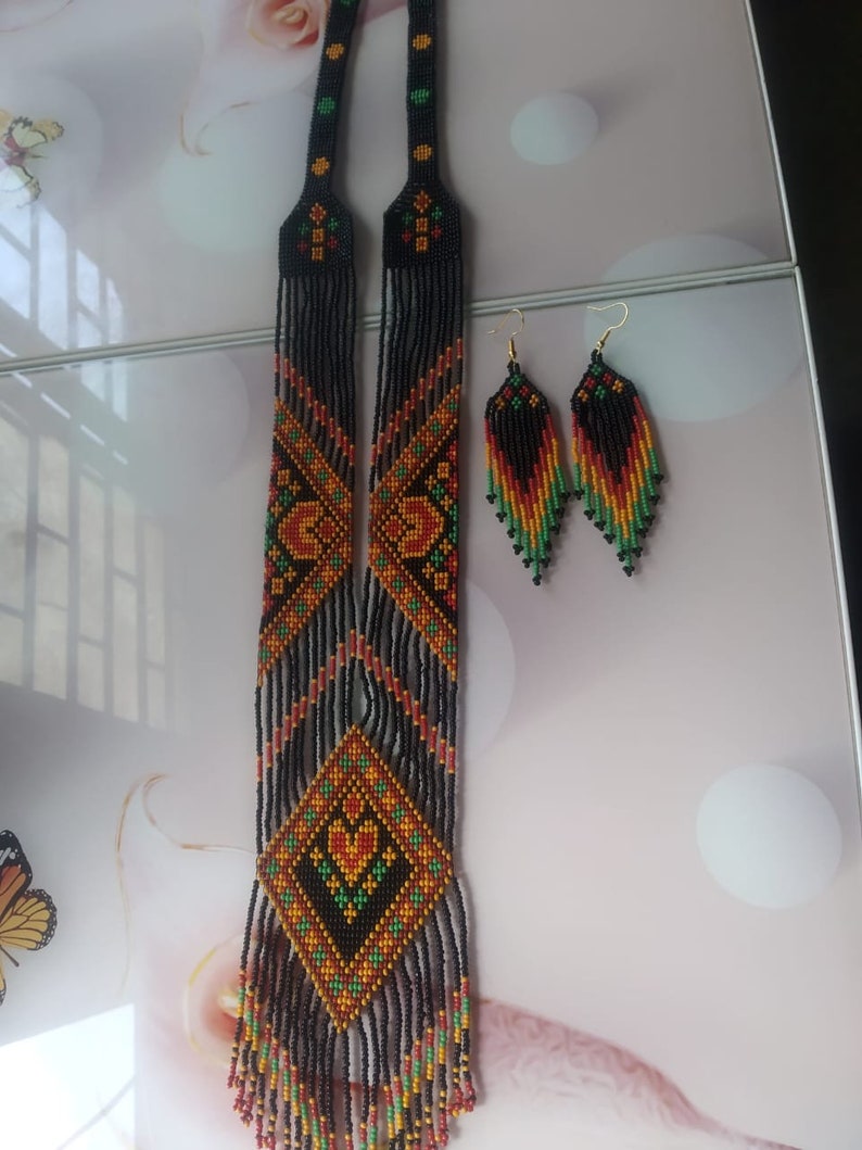 May include: A long black beaded necklace with orange, red and green geometric patterns and matching earrings. The necklace has a fringe of beads at the bottom.