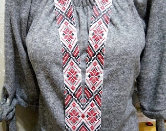 May include: A beaded necklace with a geometric pattern in red, black, and white. The necklace has a long, vertical design with a fringe at the bottom. The beads are small and tightly woven, creating a detailed pattern.