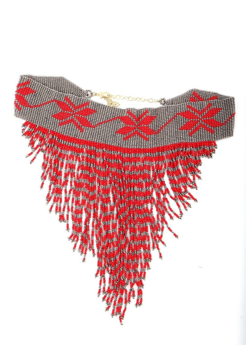 Peut inclure: Un collier de perles rouge et argent avec un design en frange. Le collier a un motif g&eacute;om&eacute;trique avec des fleurs rouges sur un fond argent&eacute;.