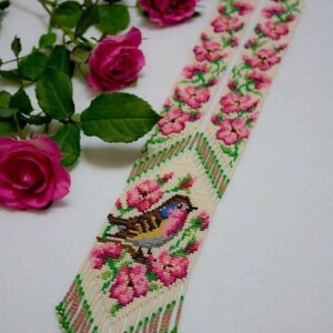 May include: A white beaded necklace with a pink and green floral design and a small bird in the center. The necklace has a fringe at the bottom. The text "Alena Fedorova with love" is at the bottom of the image.
