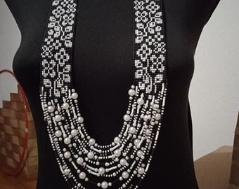 May include: A long, multi-strand necklace made of white beads and black beads woven into a floral pattern.