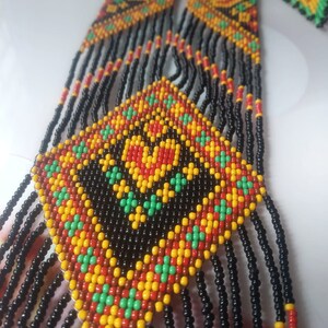 May include: A long beaded necklace with a geometric pattern in black, red, yellow, and green. The necklace has a fringe of black beads.