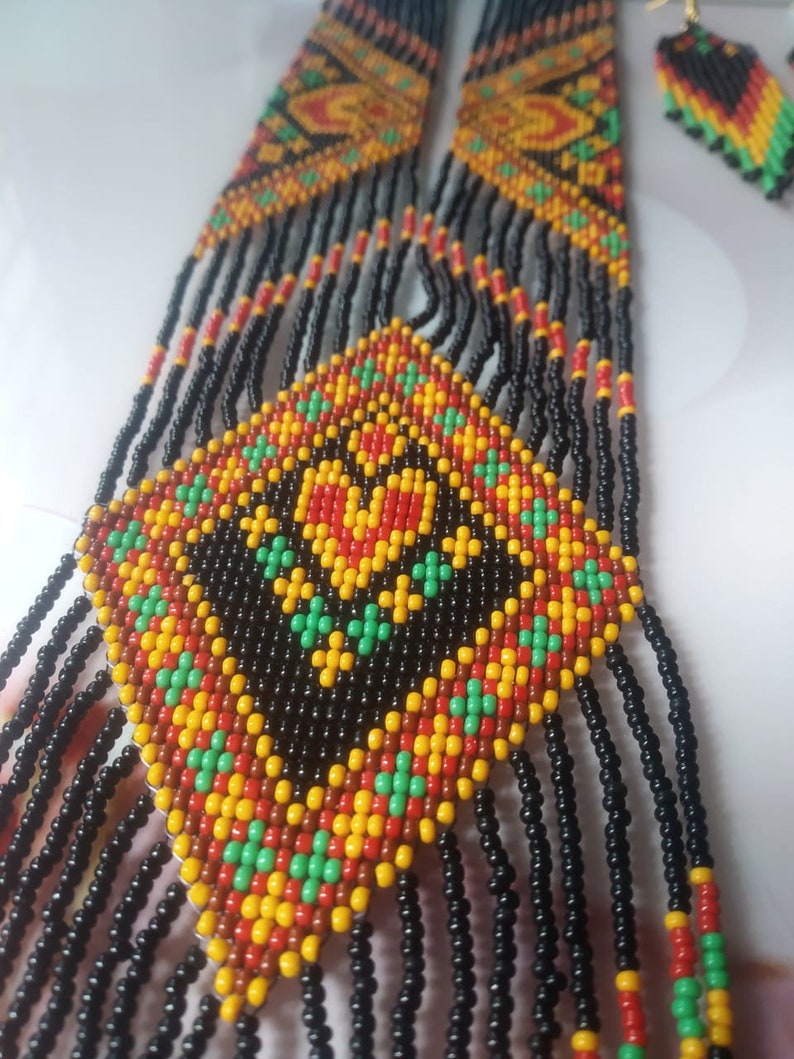 May include: A long beaded necklace with a geometric pattern in black, red, yellow, and green. The necklace has a fringe of black beads.