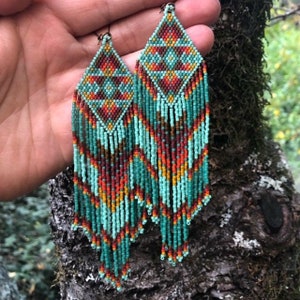 Könnte beinhalten: Türkise, orangefarbene und braune Perlenohrringe mit geometrischem Muster. Die Ohrringe sind lang und hängen herunter.