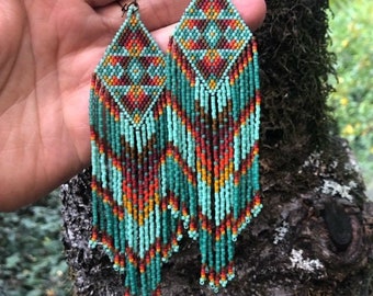 May include: Teal, orange, and brown beaded earrings with a geometric pattern. The earrings are long and dangle.