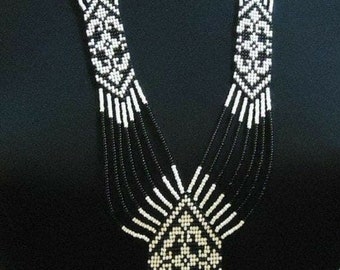 May include: A multi-strand beaded necklace with a geometric pattern in black and white. The necklace is made of small beads and has a long, flowing design.