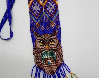 May include: A beaded necklace featuring a colourful owl design and fringe. The owl is brown, with yellow eyes and a blue background. The fringe is blue, gold and green.