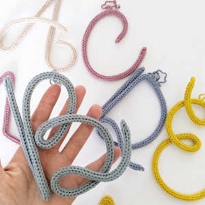 May include: A set of five crocheted letters, each in a different colour. The letters are 'A', 'C', 'D', 'E', and 'S'. The letters are made with a chunky yarn and are a great addition to a nursery or child's room.