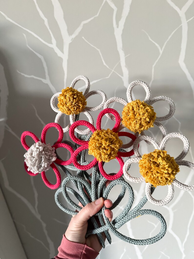 Op de afbeelding: Een boeket van vijf gehaakte bloemen met pompoenen in tinten wit, grijs en geel. De bloemen zijn verbonden door een grijze gehaakte steel.