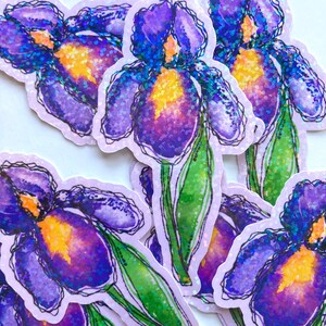 May include: A collection of stickers featuring a watercolor illustration of a purple iris flower with a yellow center and green stem. The stickers have a glittery, holographic effect and a light purple border. The design is a floral theme.