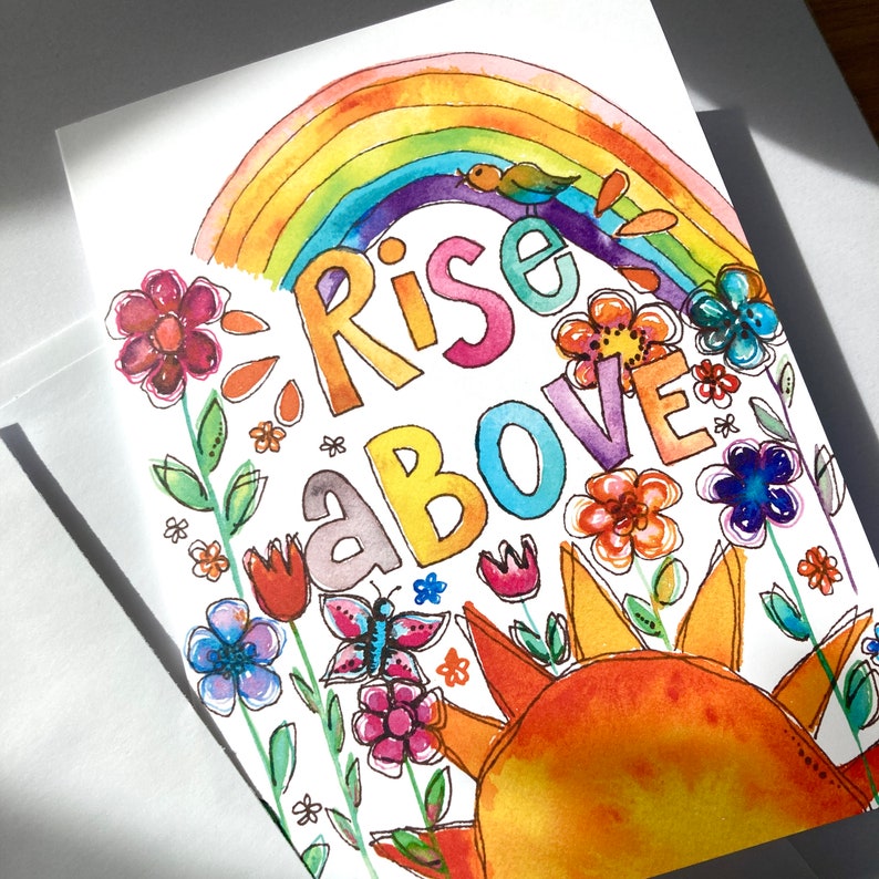 May include: Watercolor greeting card with a rainbow, sun, flowers, and the words "Rise Above." The design features a colorful rainbow arching over the words, with a small bird perched on top. The card is decorated with various flowers and a butterfly.