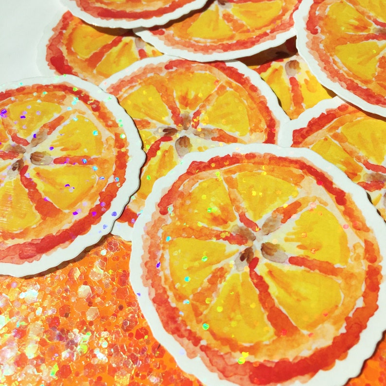 Puede incluir: Pegatinas de acuarela de rodajas de naranja con tonos amarillos y naranjas, y un contorno rojo. Las pegatinas tienen un efecto brillante e iridiscente. Las pegatinas est&aacute;n esparcidas sobre una superficie con purpurina naranja.