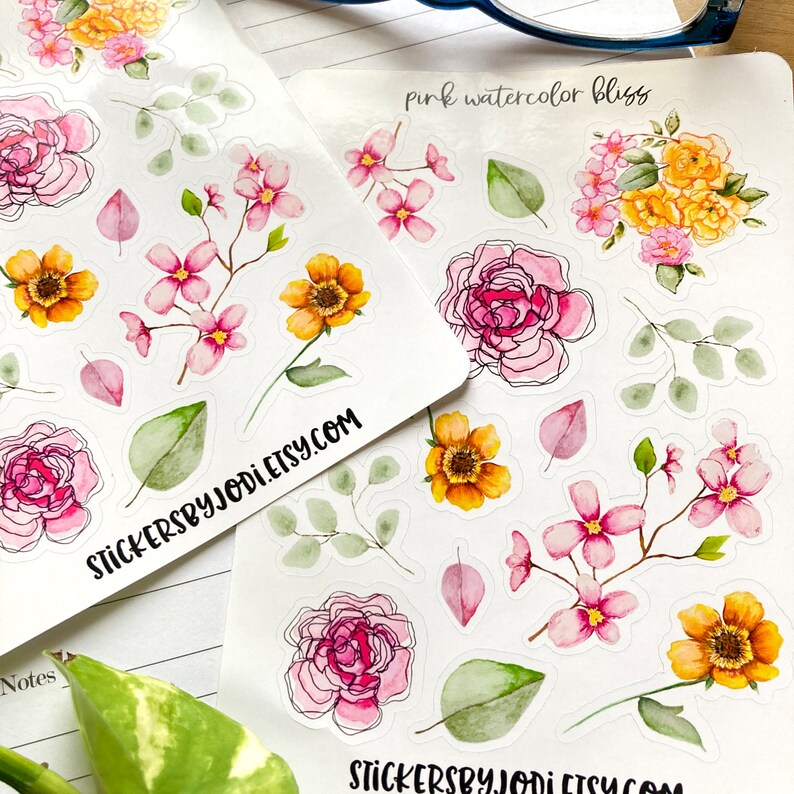 May include: Two sheets of floral stickers featuring watercolor designs. The stickers include pink and yellow flowers, green leaves, and the text "pink watercolor bliss" and "stickersbyjodi.etsy.com".