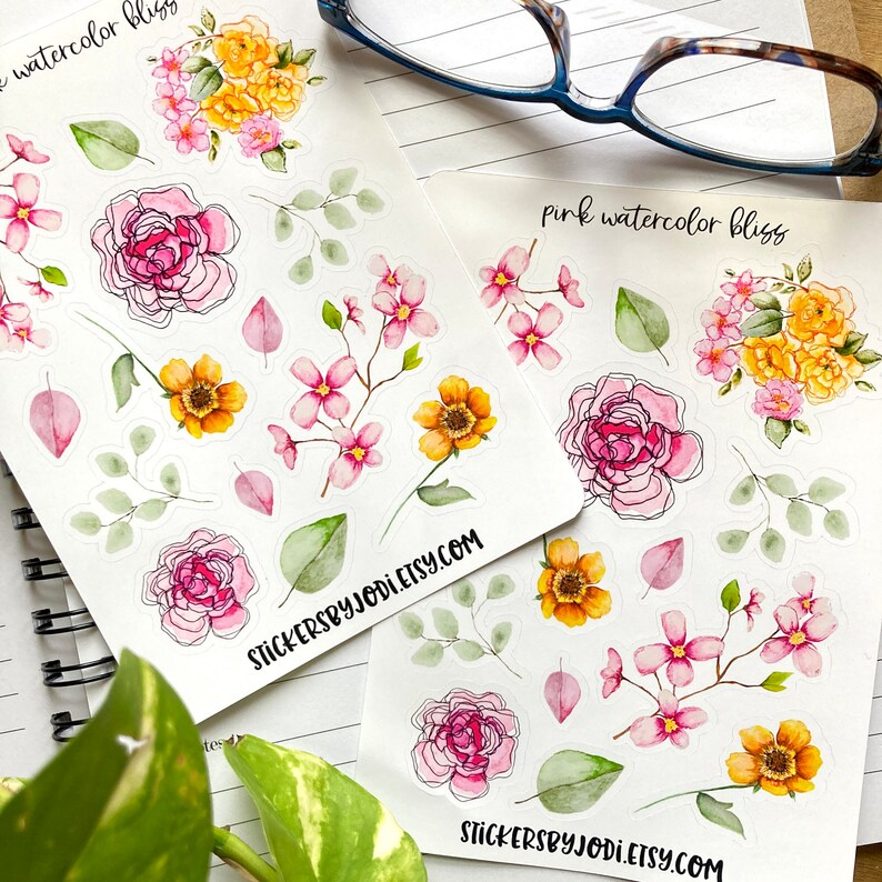 May include: Two sheets of floral stickers featuring watercolor designs. The stickers include pink and yellow roses, small pink flowers, green leaves, and the text "pink watercolor bliss" and "stickersbyjodi.etsy.com". The stickers are on a white background.